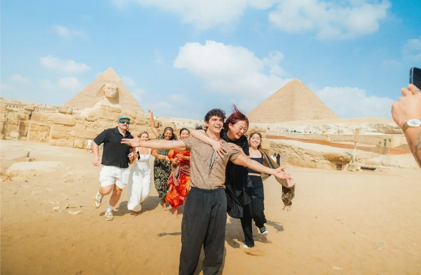 A cheerful group of tourists taking photos in front of the Great Sphinx and Pyramids of Giza during a trip to Egypt in January.