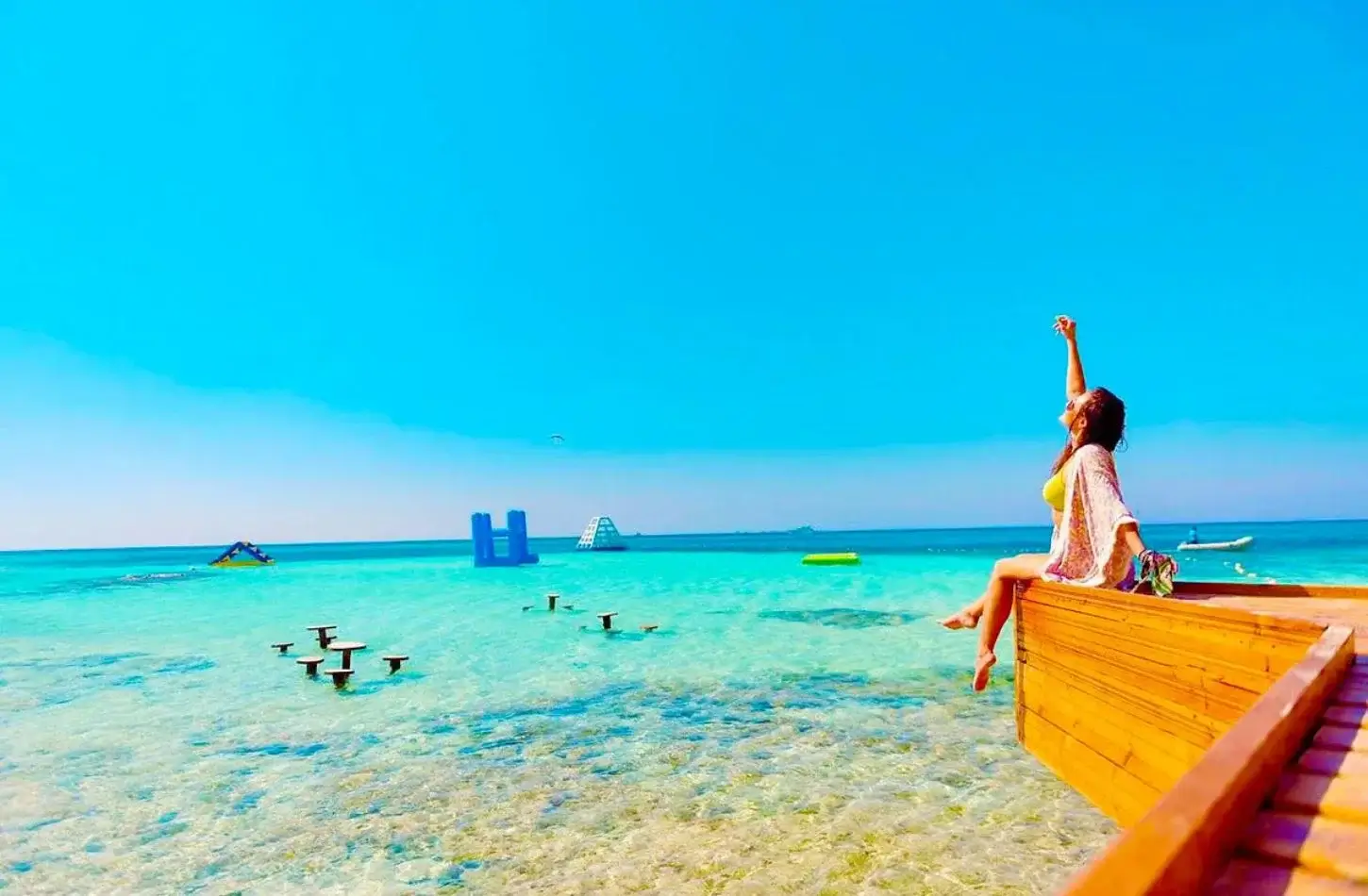 Woman sitting on a wooden pier overlooking crystal-clear turquoise waters at Orange Bay Island in Hurghada during a trip to Egypt in January.